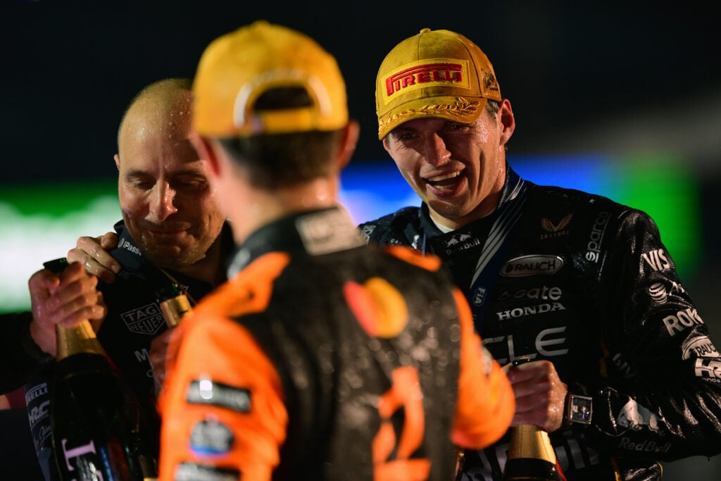 Max Verstappen laughing as he looks at Lando Norris on the podium of the 2025 Las Vegas Grand Prix, with his Red Bull race engineer, Gianpiero Lambiase, alongside him.