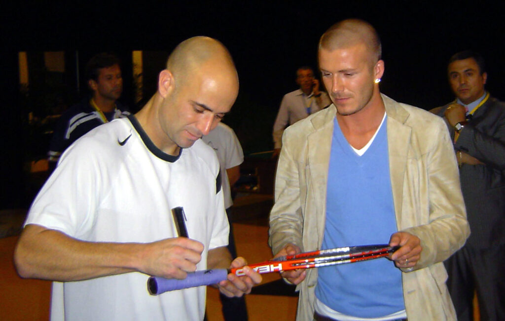 Andre Agassi of the USA signs a tennis racquet for David Beckham during the ATP Madrid Masters at the Nuevo Rockodromo on October 21, 2004 in Madrid, Spain.