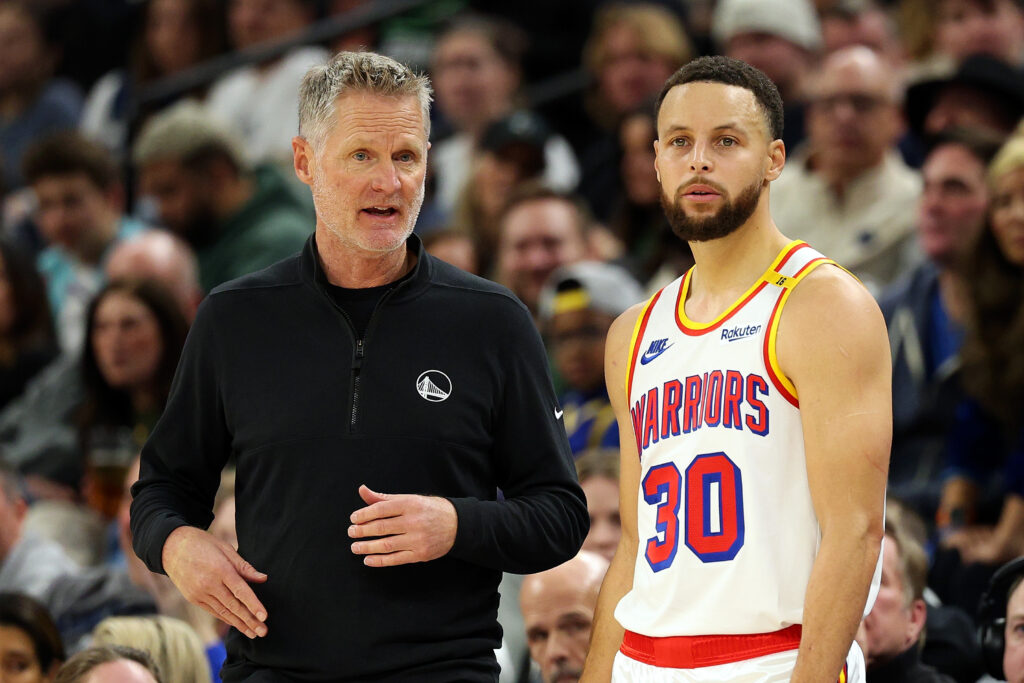 Head coach Steve Kerr talks to Stephen Curry #30 of the Golden State Warriors in the second quarter of the game against the Minnesota Timberwolves at Target Center on December 21, 2024 in Minneapolis, Minnesota.