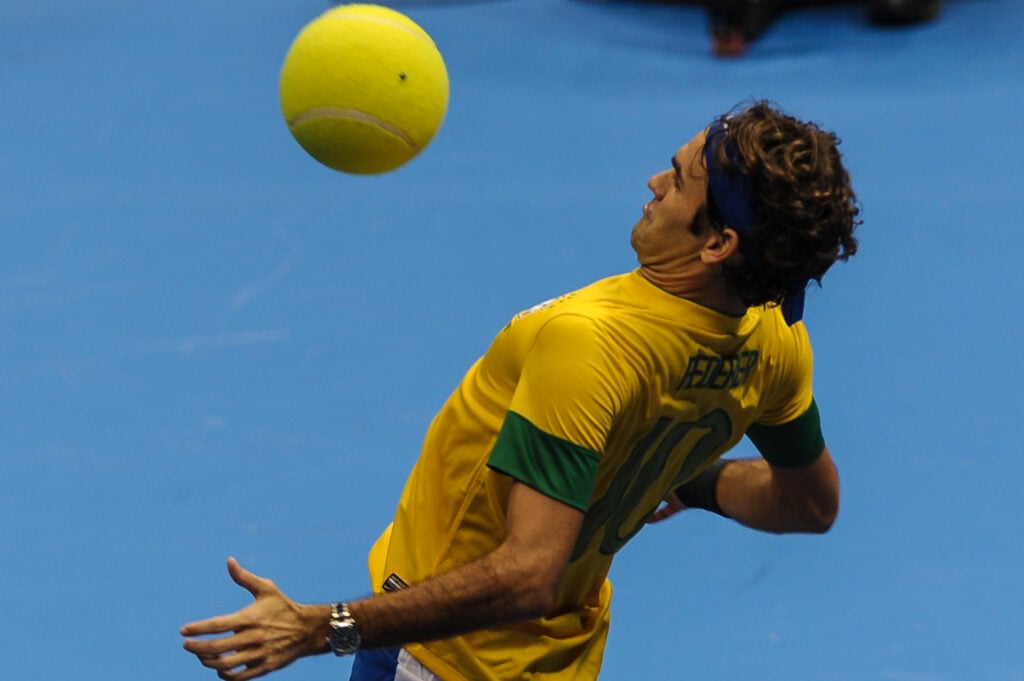 Swiss tennis player Roger Federer, wearing a Brazilian national football team uniform, controls a giant tennis ball during an exhibition match against German Tommy Haas