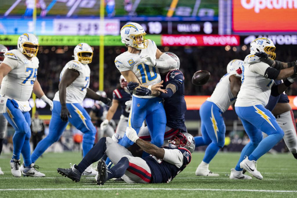 Justin Herbert #10 of the Los Angeles Chargers fumbles as he's tackled by New England Patriots line backer Anfernee Jennings (33) during an NFL wild card playoff game