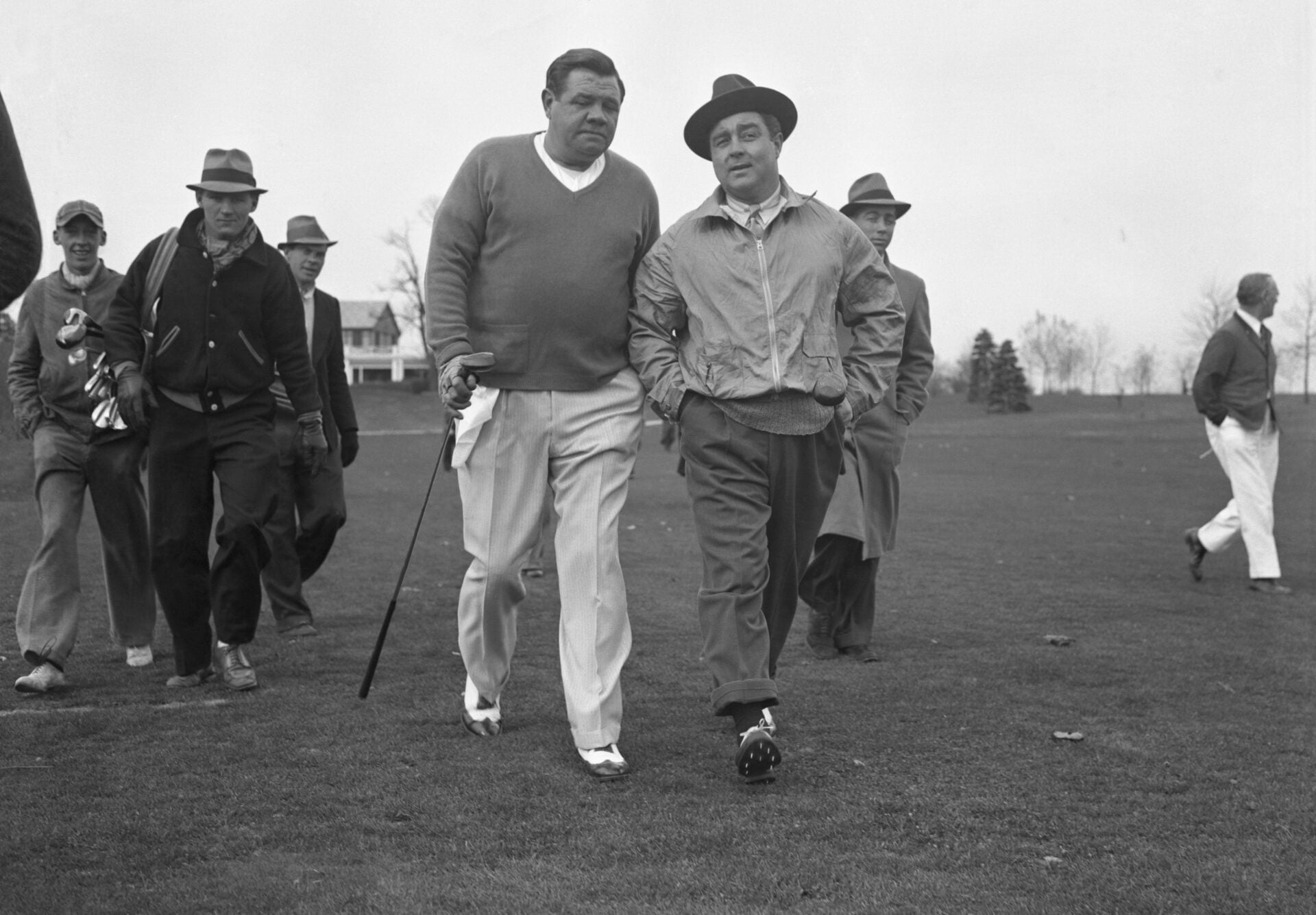 A picture of Babe Ruth, former Baseball great and now no mean golfer, walking down toward the first hole with John Montague. The two men played nin...