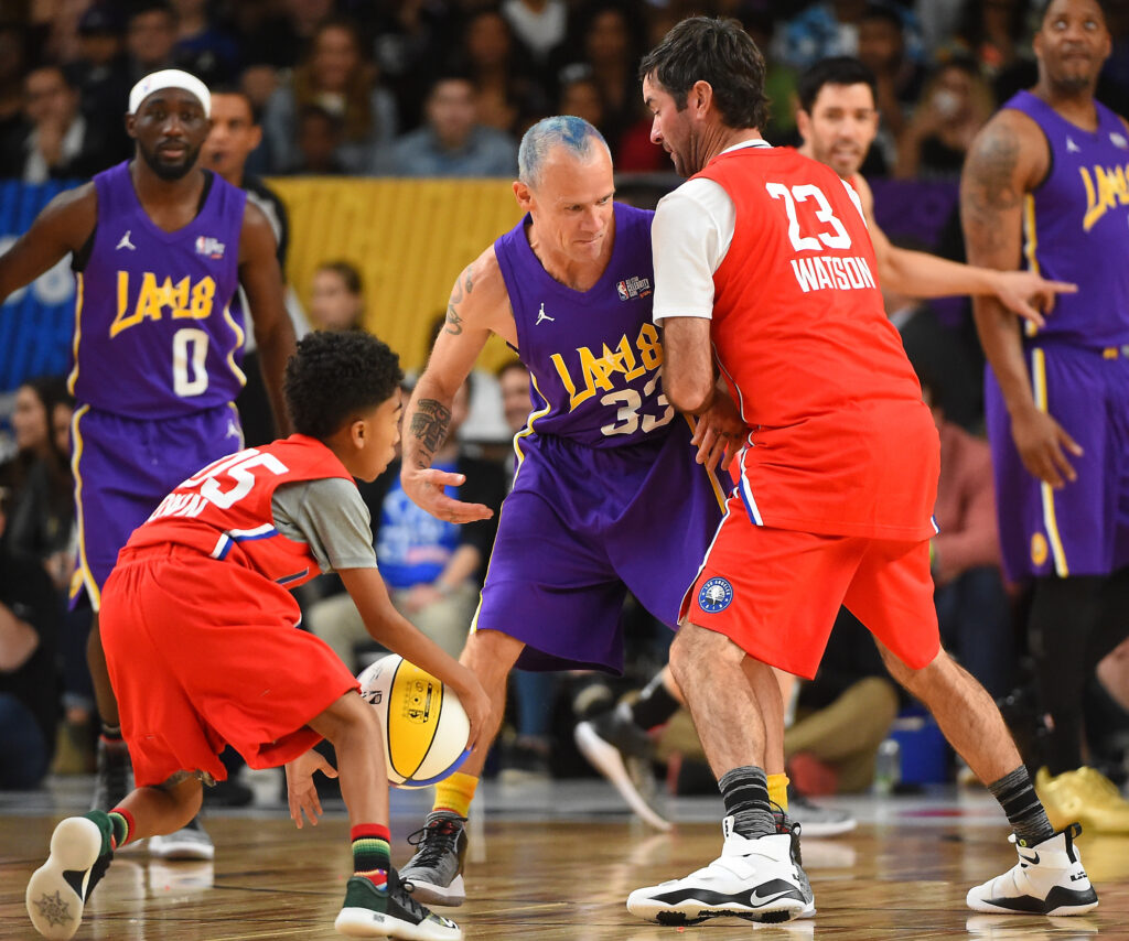 Professional golfer Bubba Watson sets a pick on Flea of the rock band Red Hot Chili Peppers, as actor Miles Brown drives to the basket during the 2018 NBA All-Star Game Celebrity Game