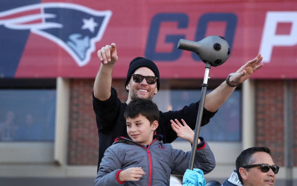 New England Patriots quarterback Tom Brady and his son wave to the crowd during the New England Patriots Super Bowl LIII victory parade in Boston on Feb. 5, 2019. Trainer Alex Guerrero is at bottom right.