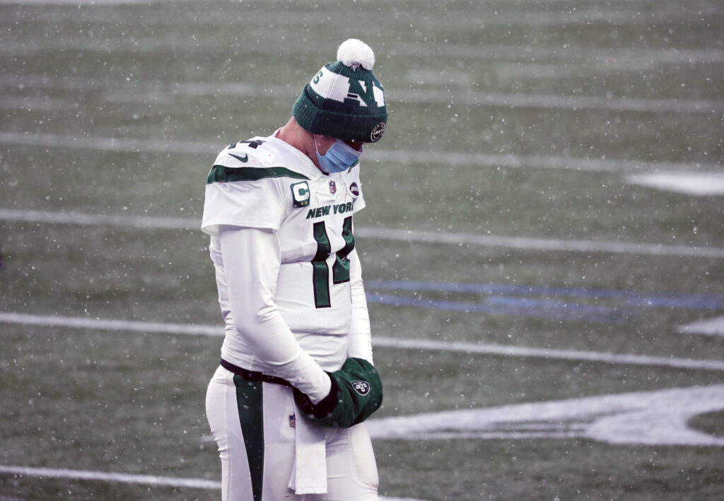Sam Darnold #14 of the New York Jets wears a protective face mask and hangs his head as he exits the field in the snow against the New England Patriots at Gillette Stadium on January 3, 2021 in Foxborough, Massachusetts.