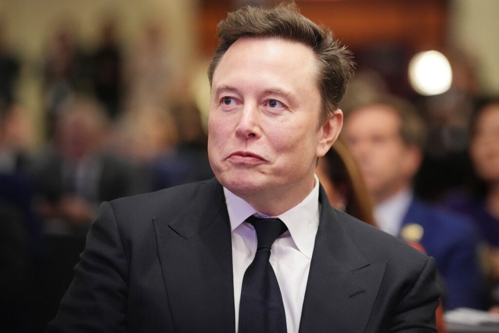 Elon Musk listens as U.S. President-elect Donald Trump addresses a House Republicans Conference meeting at the Hyatt Regency on Capitol Hill.