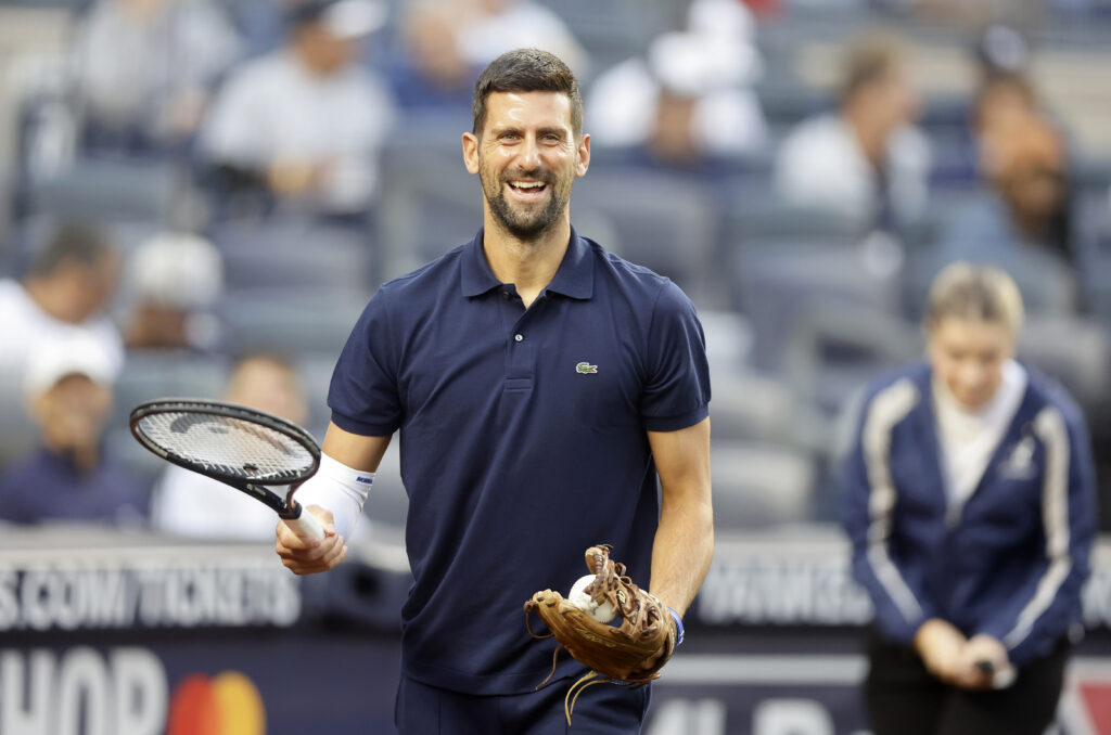 Tennis player Novak Djokovic has a laugh carrying his tennis racquet before throwing the ceremonial first pitch prior to a game between the New York Yankees and Boston Red Sox at Yankee Stadium on August 21, 2025 in New York City.