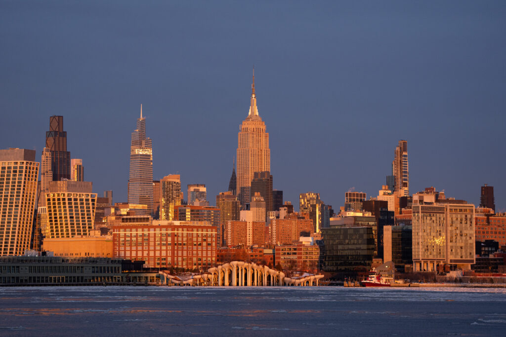 Ice floes drift along the Hudson River as the sun sets over New York City, casting warm hues across the frozen waterway on February 01, 2026 in United States. At the same time, the full Snow Moon rises behind the Empire State Building.