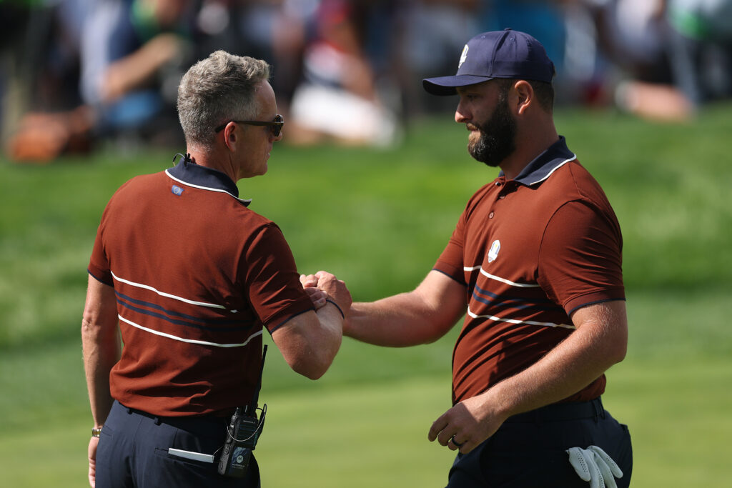 Captain Luke Donald and Jon Rahm of Team Europe show camaraderie on the 16th green during the Saturday morning foursomes matches of the 2025 Ryder Cup