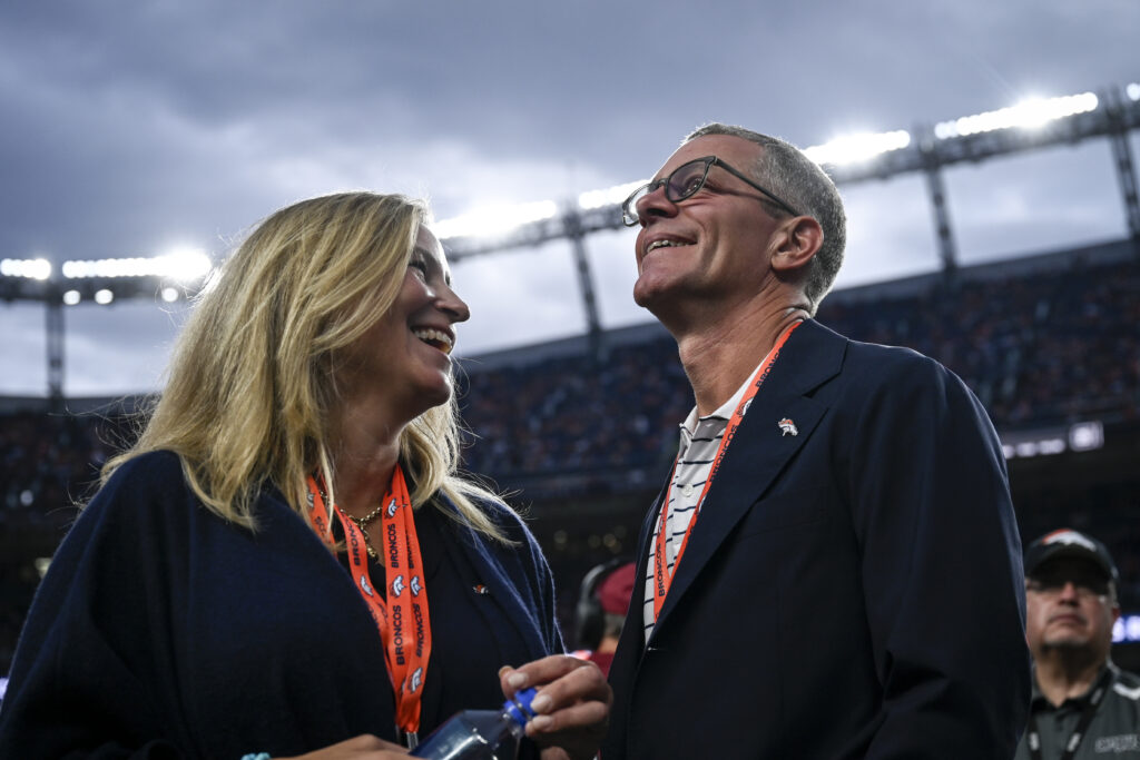 Carrie Walton Penner and Greg Penner of the Walton Penner group talk on the sidelines during the first quarter against the Dallas Cowboys at Empower Field at Mile High.