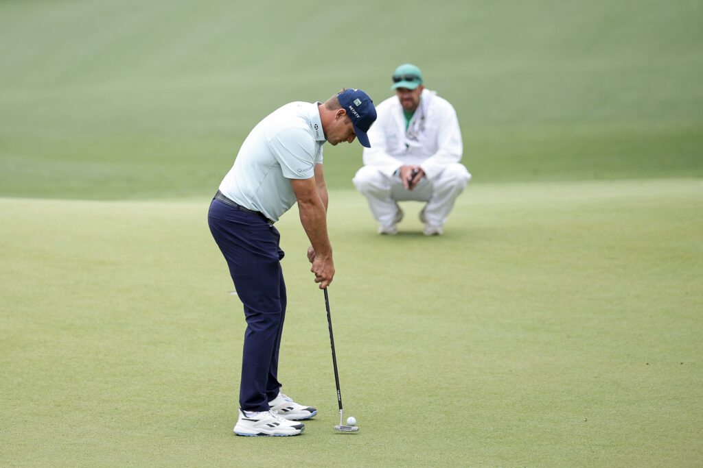 Bryson DeChambeau of the United States hits a putt as his caddie Greg Bodine looks on while playing the 14th hole during a practice round