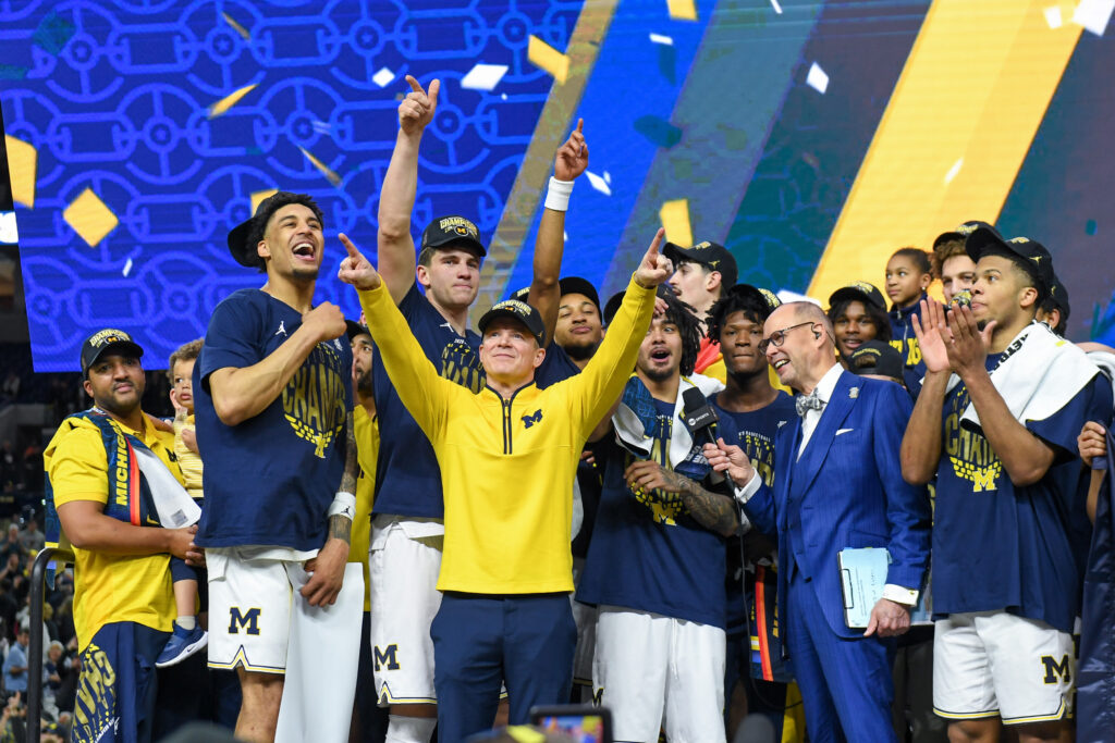 Yaxel Lendeborg #23, Will Tschetter #42, Head Basketball Coach Dusty May, and Elliot Cadeau #3 of the Michigan Wolverines celebrate with teammates after winning the 2026 NCAA Men's Basketball Tournament national championship game against the UConn Huskies at Lucas Oil Stadium.