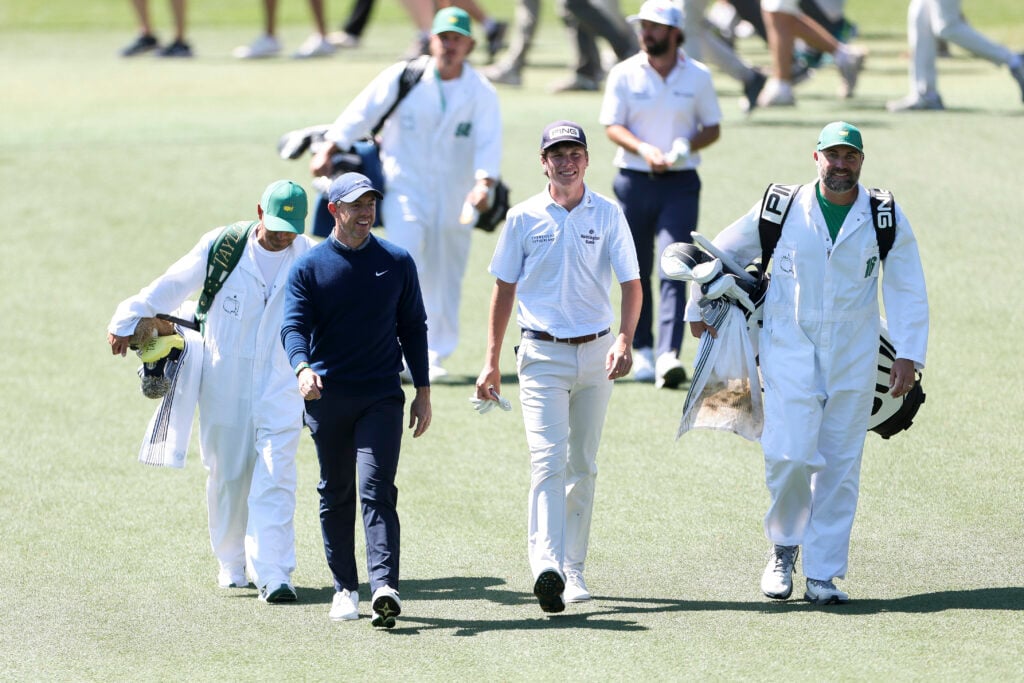 Rory McIlroy and Mason Howell walk up the fairway during the first round of The Masters