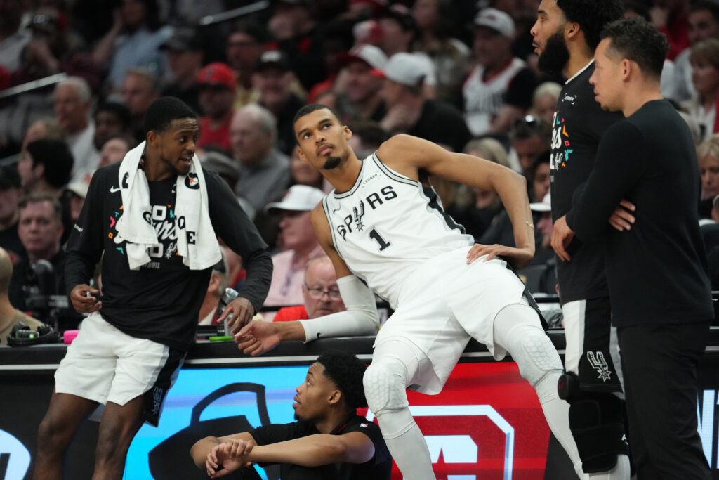 De'Aaron Fox #4 and Victor Wembanyama #1 of the San Antonio Spurs talk at the scorer's table during the second half of Game Four of the Western Conference First Round Playoffs