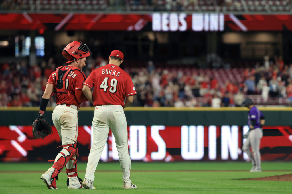 Tyler Stephenson #37 and Brock Burke #49 of the Cincinnati Reds celebrate as Jordan Beck #27 of the Colorado Rockies walks off the field after a game at Great American Ball Park.