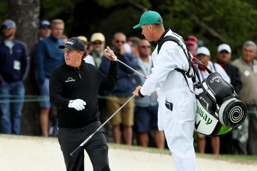 Phil Mickelson takes a club from caddie Jim Mackay on the first hole during the first round of the 2017 Masters at Augusta National