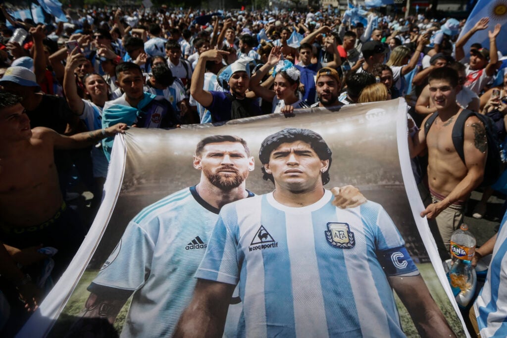 Fans of Argentina hold a flag depicting Argentine football stars Lionel Messi (L) and late Diego Maradona (R) while gathering at the Obelisk to celebrate winning the Qatar 2022 World Cup against France in Buenos Aires, on December 18, 2022.