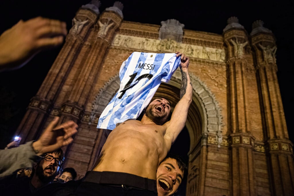 An Argentinian man holds up another man with a Lionel Messi