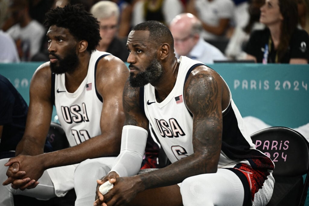 USA's #11 Joel Embiid (L) and USA's #06 LeBron James react from the bench in the men's semifinal basketball match between USA and Serbia during the Paris 2024 Olympic Games at the Bercy Arena.