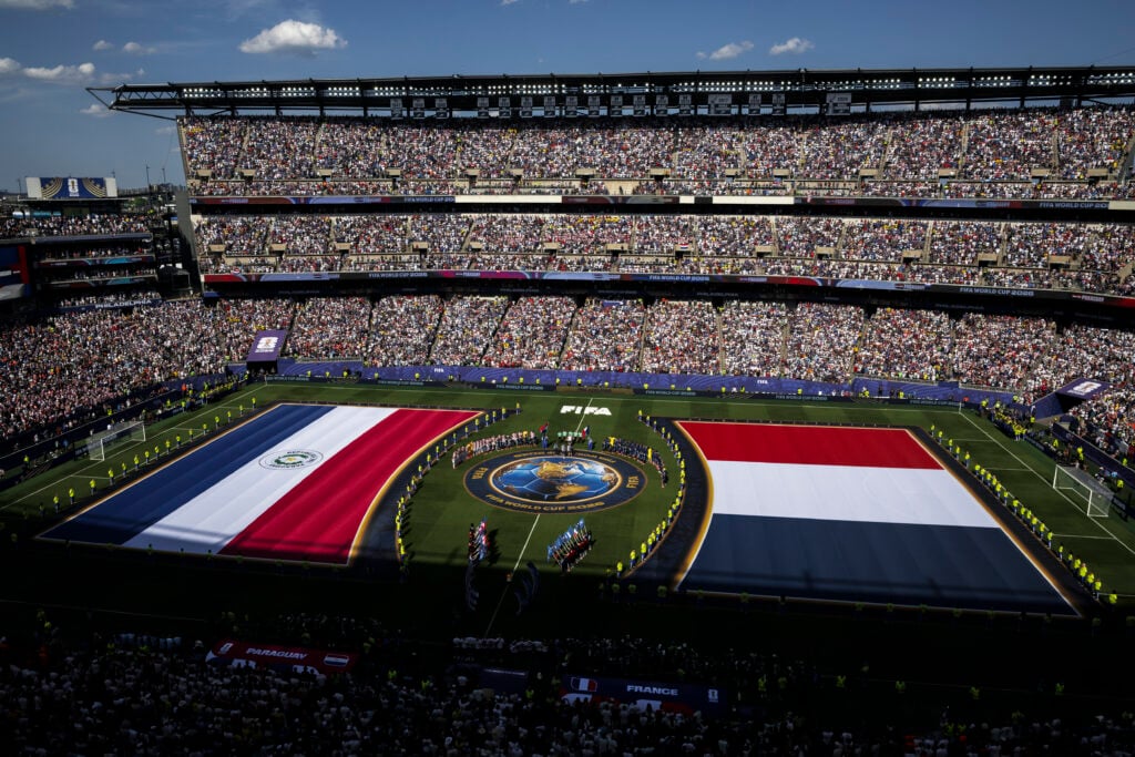 Players and officials line up as two large flags are displayed on the pitch during the national anthems prior to the FIFA World Cup 2026 Round of 16 football match between Paraguay and France